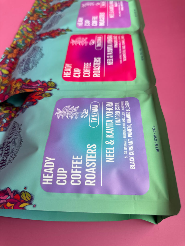 Three coffee bags with colorful labels on a pink background