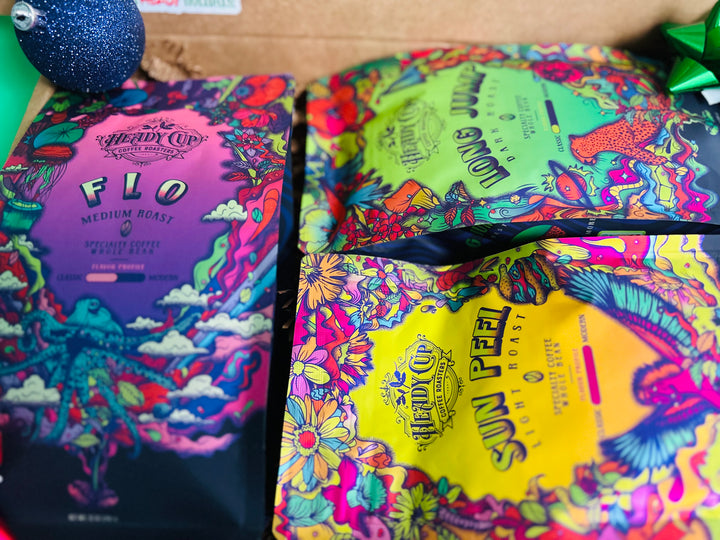 A picture of two colorful Heady Cup Coffee Roasters bags in a three blend gift box