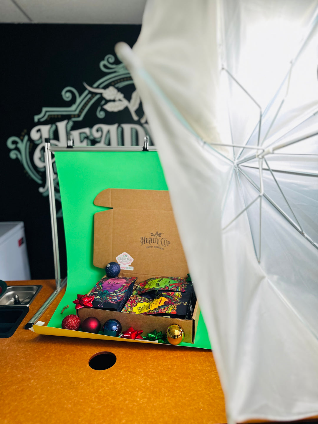 A picture of two colorful Heady Cup Coffee Roasters bags in a three blend gift box behind the scenes