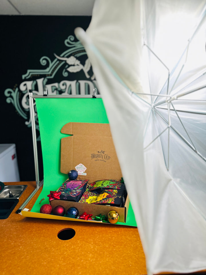 A picture of two colorful Heady Cup Coffee Roasters bags in a three blend gift box behind the scenes