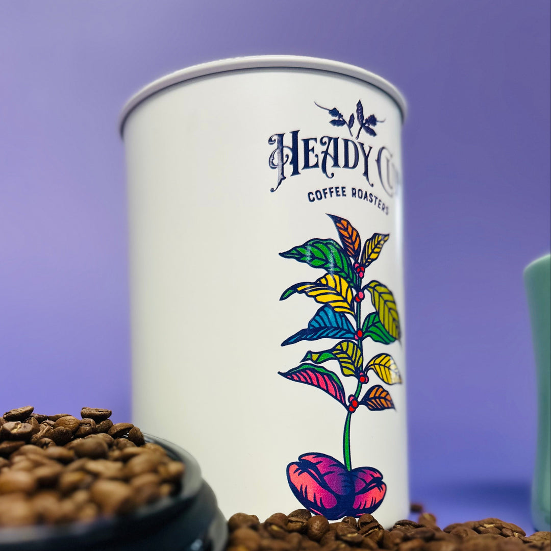 White coffee canister with colorful Heady Cup Coffee Roasters leaf design on a purple background