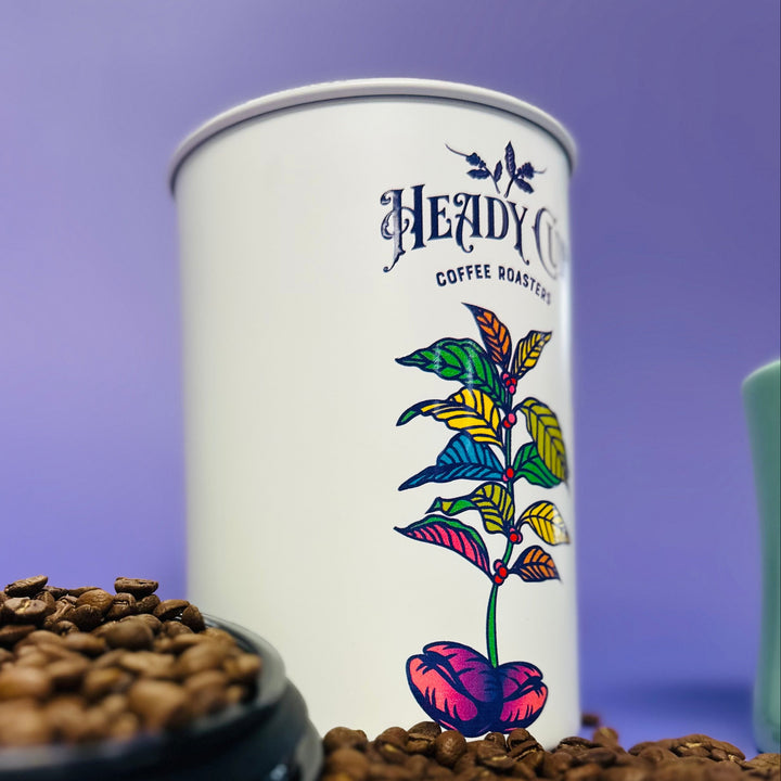 White coffee canister with colorful Heady Cup Coffee Roasters leaf design on a purple background