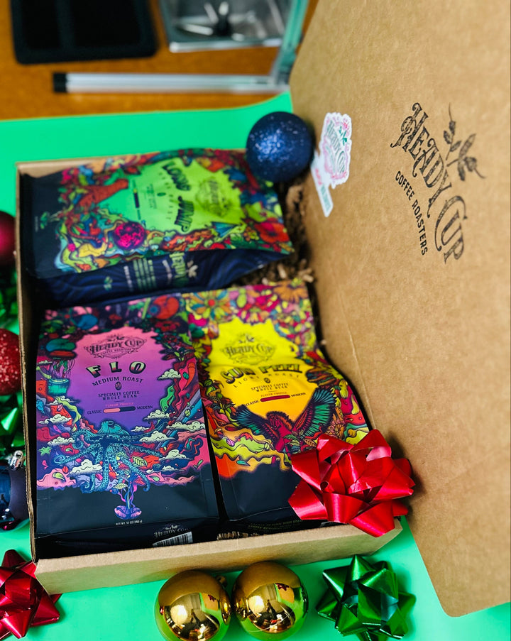 A picture of two colorful Heady Cup Coffee Roasters bags in a  three blend gift box
