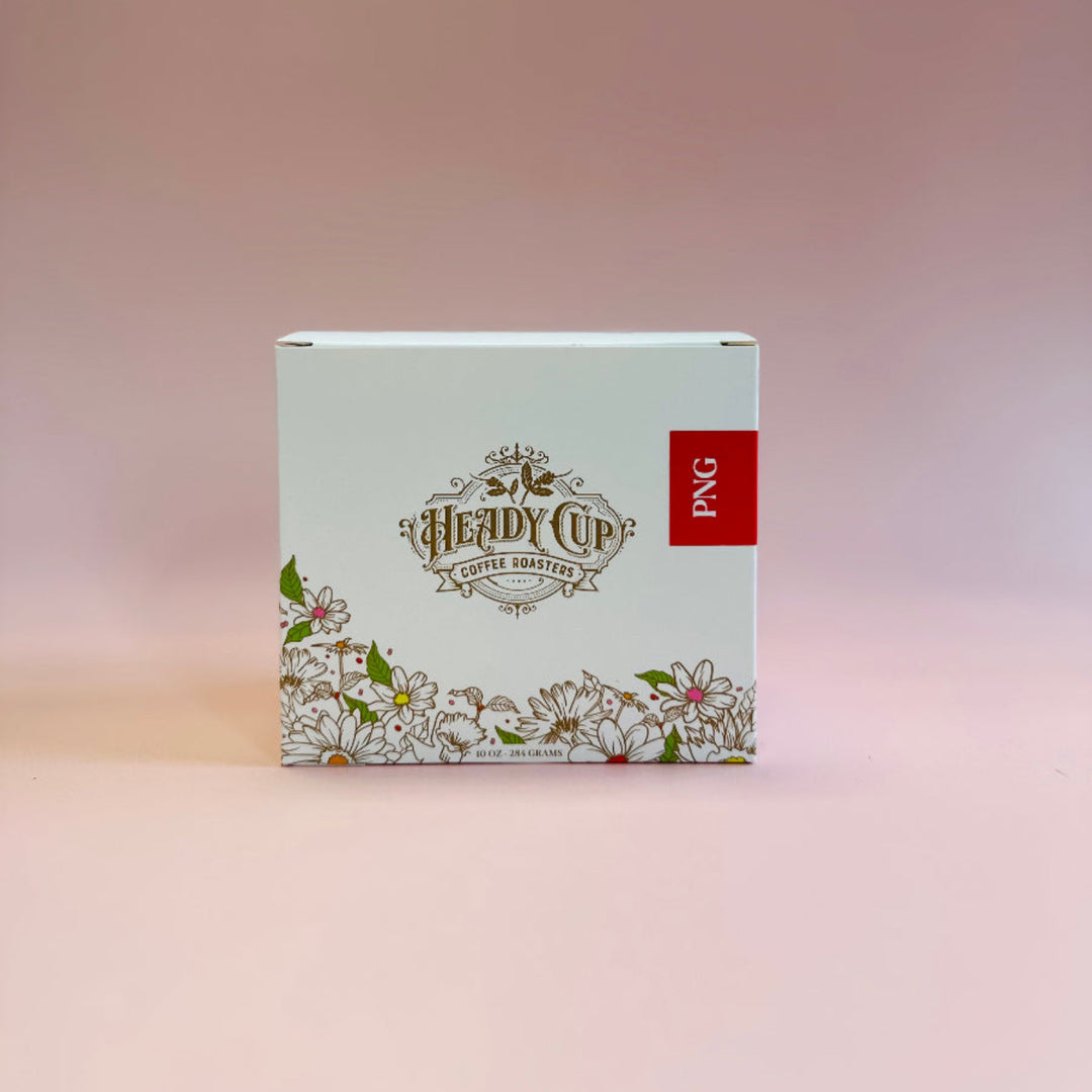 A square product box for 'Heady Cup Coffee Roasters' featuring a white background, delicate floral line art along the bottom, and a small red vertical label on the right side that reads 'PNG'. The box is centered against a soft pink gradient background.