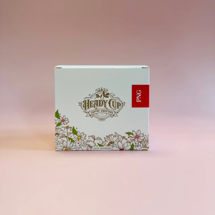 A square product box for 'Heady Cup Coffee Roasters' featuring a white background, delicate floral line art along the bottom, and a small red vertical label on the right side that reads 'PNG'. The box is centered against a soft pink gradient background.