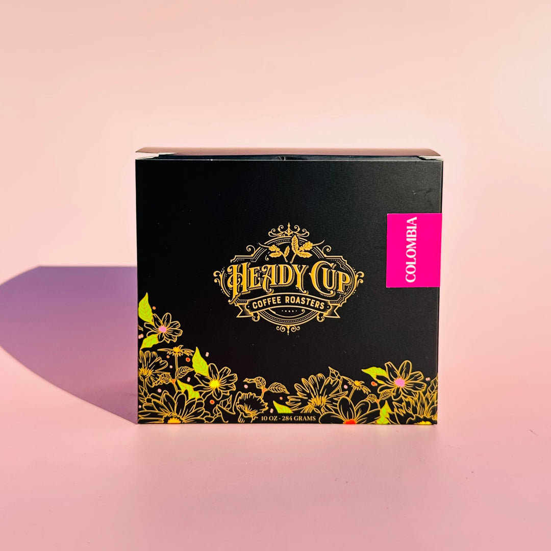 A black Heady Cup Coffee Roasters Zaza Collection box of Colombia Coffee. Label is magenta and box is against a pink background. 