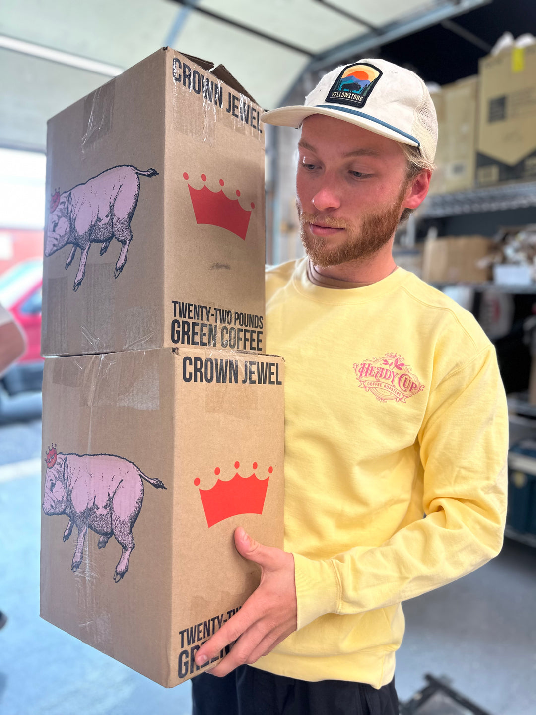 Jack holding two boxes of Heady Zaza Coffee while wearing a yellow Heady Cup Coffee Roaster definition sweatshirt. 