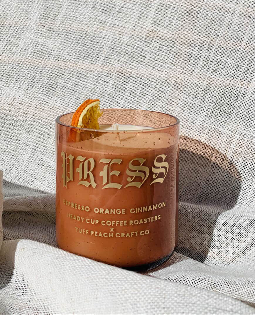 Picture of a Heady Cup Coffee Roasters x Tuff Peach Craft Co. Candle on a grey background. Espresso, Orange and Cinnamon label by Ninety Two Creative. 