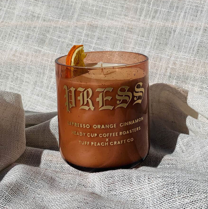 Picture of a Heady Cup Coffee Roasters x Tuff Peach Craft Co. Candle on a grey background. Espresso, Orange and Cinnamon label by Ninety Two Creative. 