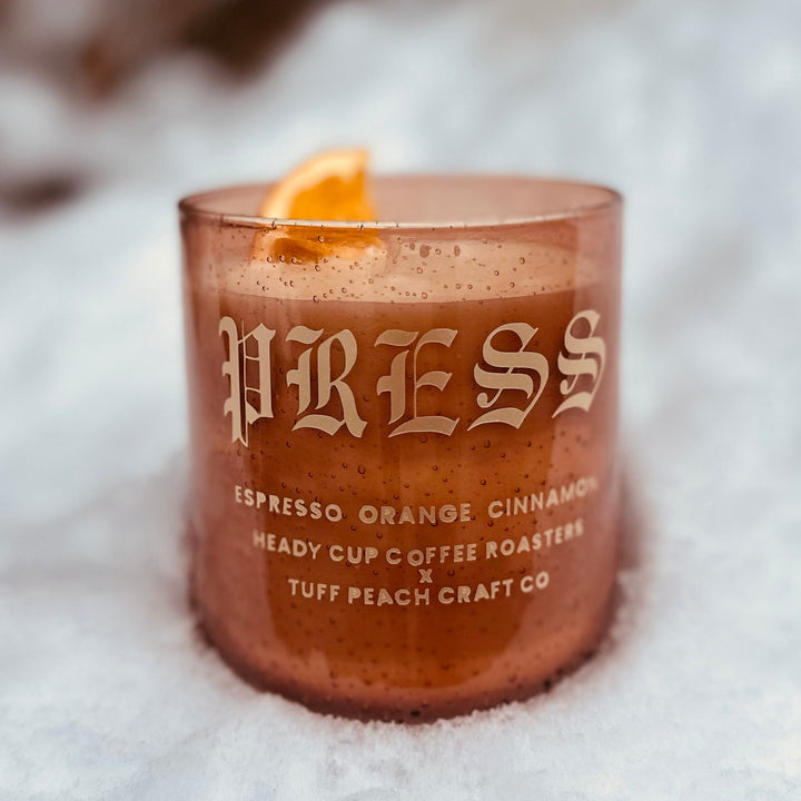 Picture of a Heady Cup Coffee Roasters x Tuff Peach Craft Co. Candle on a grey background. Espresso, Orange and Cinnamon label by Ninety Two Creative. 