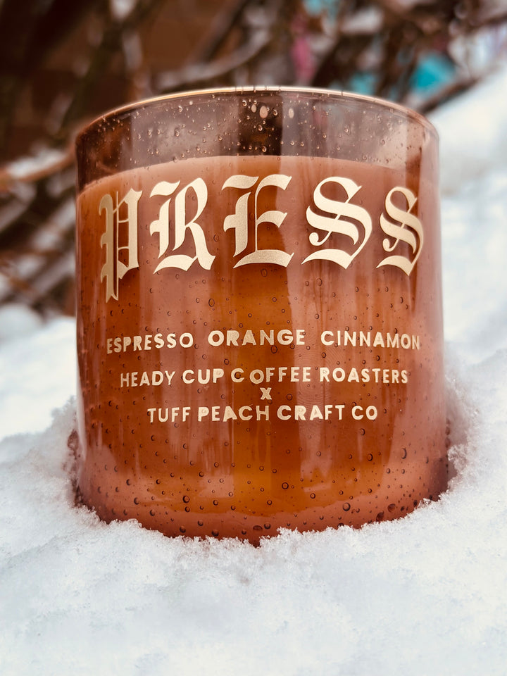 Picture of a Heady Cup Coffee Roasters x Tuff Peach Craft Co. Candle on a grey background. Espresso, Orange and Cinnamon label by Ninety Two Creative. 