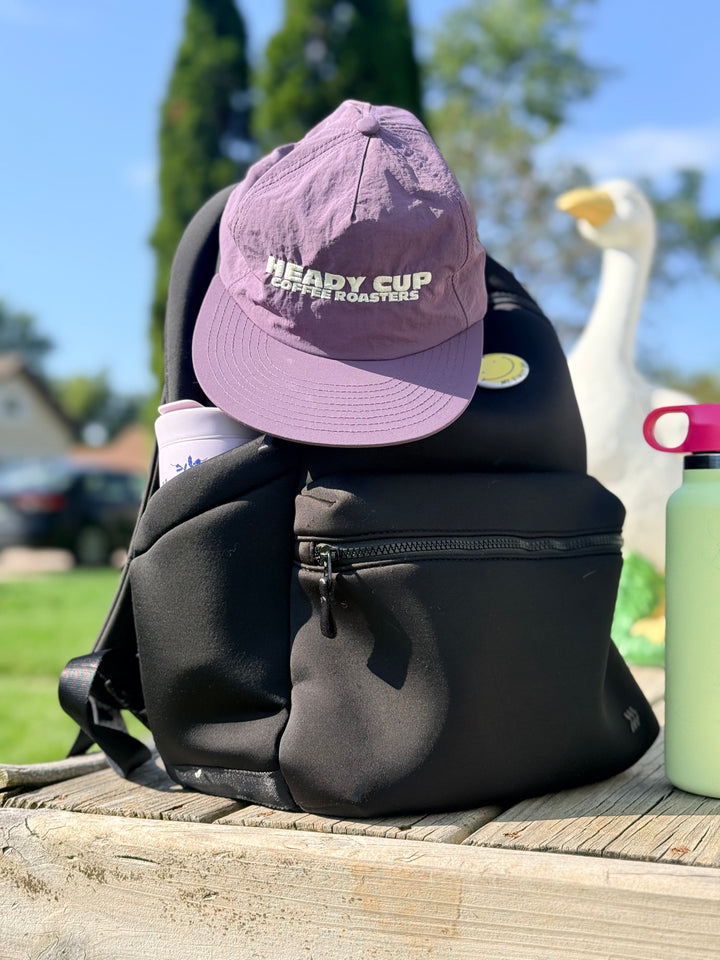 A purple Weld hat with Heady Cup Coffee Roasters embroidered on the front of the hat. A goose sits in the background. 