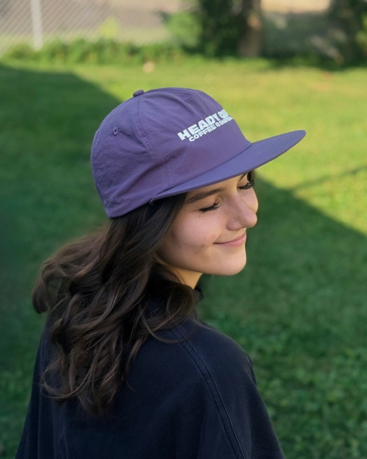 A woman wearing a purple Weld nylon hat with Heady Cup Coffee Roasters embroidered on the front of the hat. 
