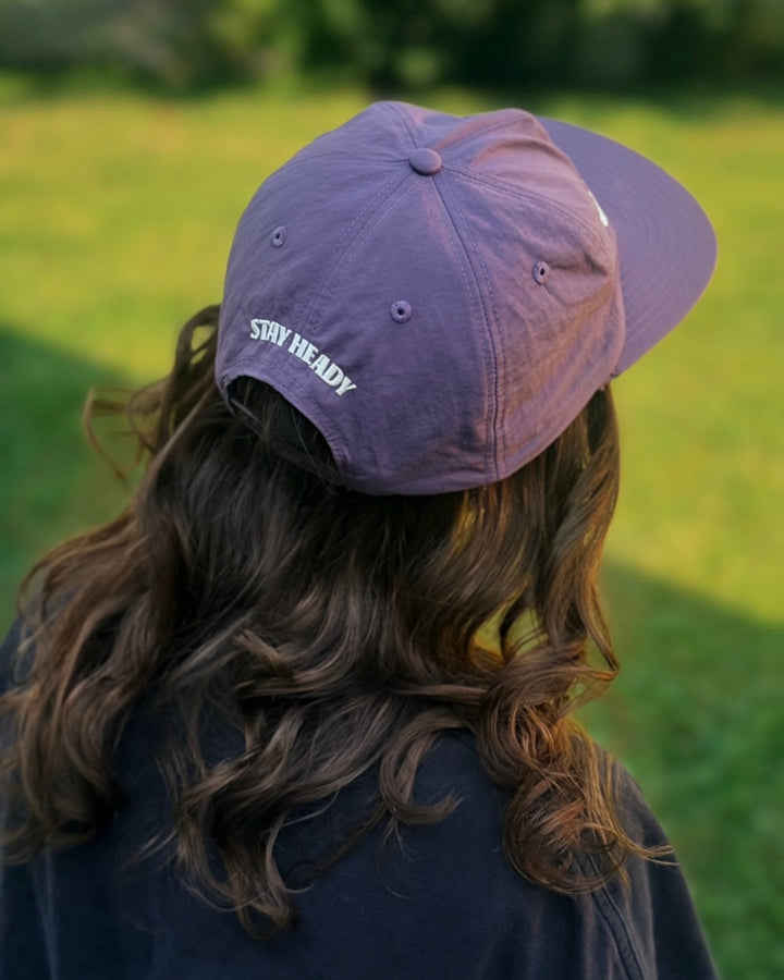 A woman wearing a purple Weld nylon hat with Heady Cup Coffee Roasters "Stay Heady" embroidered on the back of the hat. 