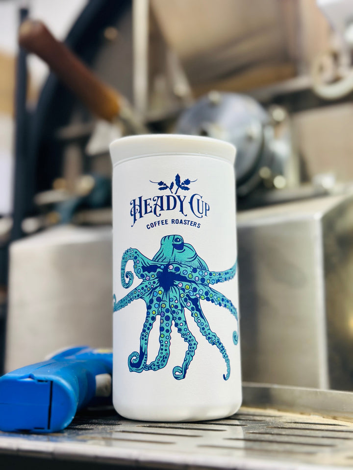 White CreatedCo NOMAD tumbler with blue octopus design and 'Heady Cup Coffee Roasters' branding in front of a coffee roaster