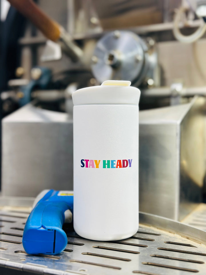 White CreatedCo NOMAD tumbler with blue octopus design and 'Heady Cup Coffee Roasters' branding in front of a coffee roaster